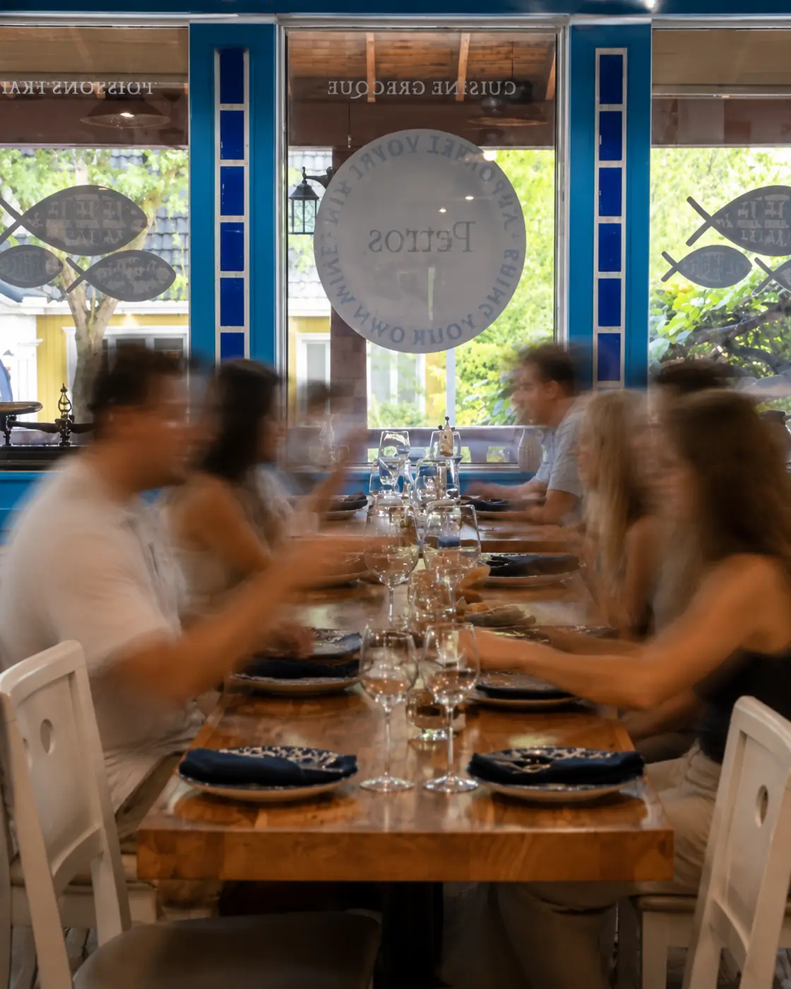 Vue à travers la vitrine Petros — Apportez votre vin — sur une longue tablée animée